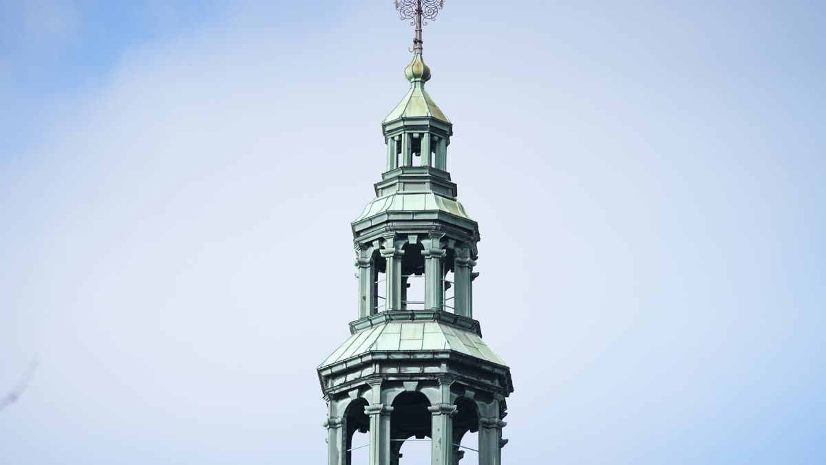 The author’s photograph of a verdigris church spire against a pale sky, standing upright: the frame this sequence straightens and cleans of dust